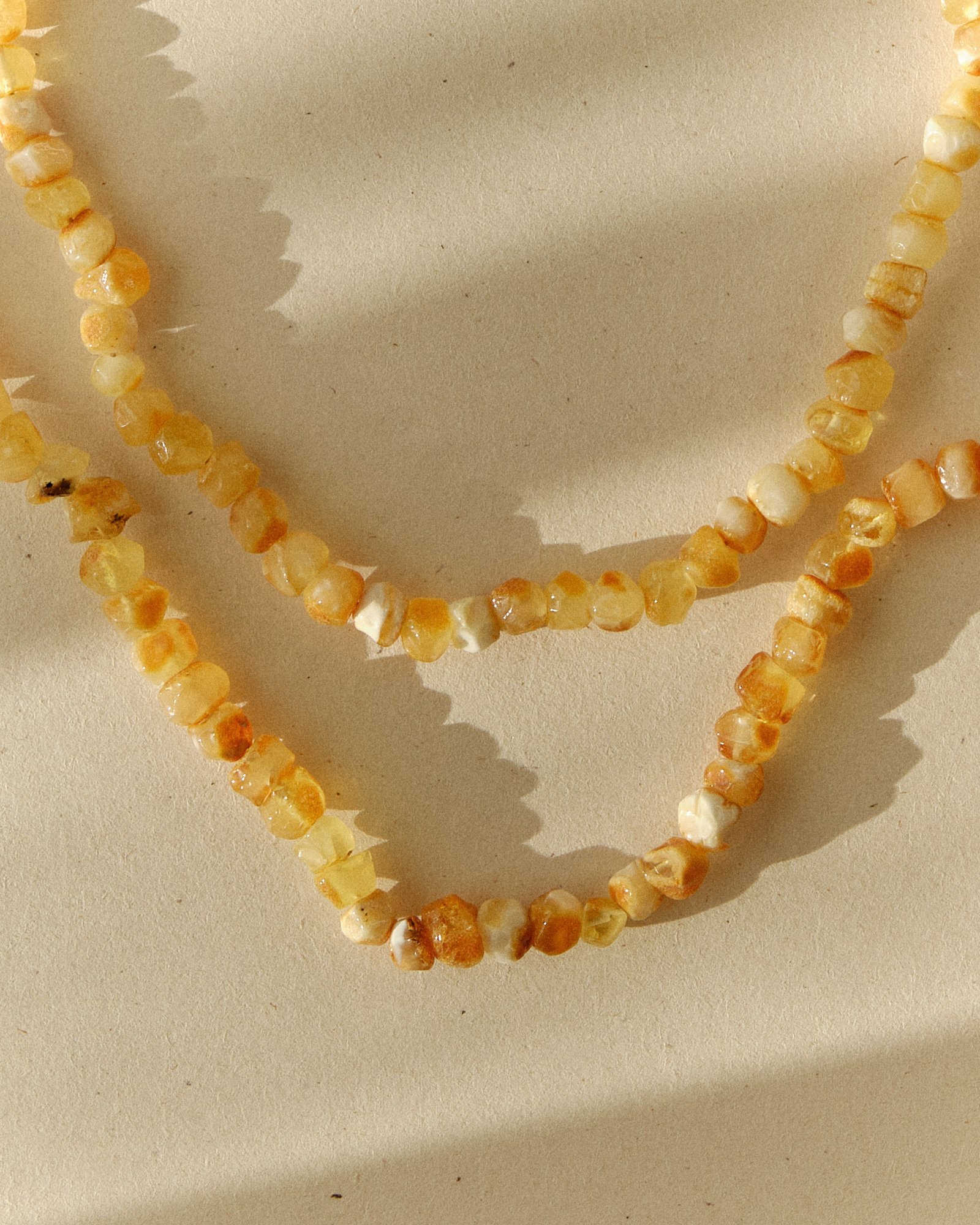 Pale butterscotch amber necklace laid in a V shape on a sunlit surface with sharp shadow