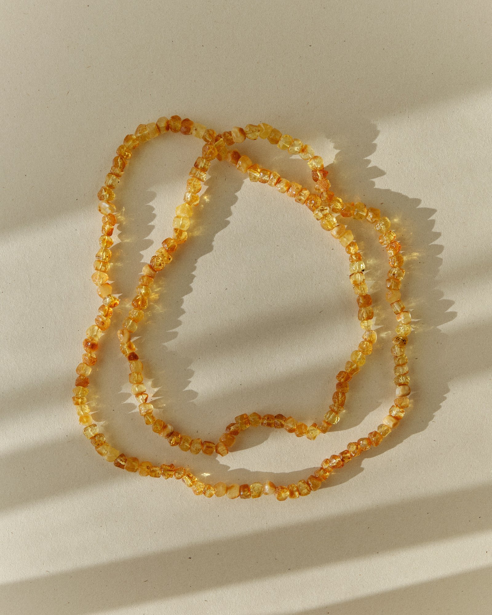 Honey amber necklace coiled loosely on a sunlit surface with sharp shadows