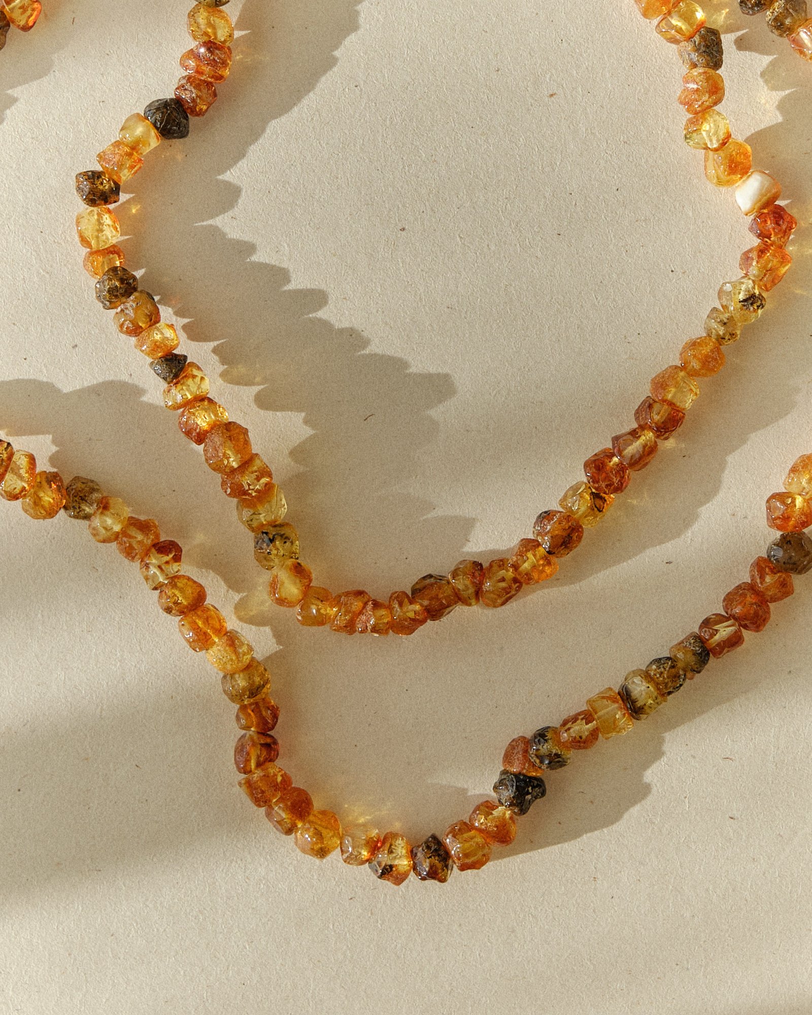 Close-up of a cognac and green amber necklace coiled on a light surface with strong raking shadow