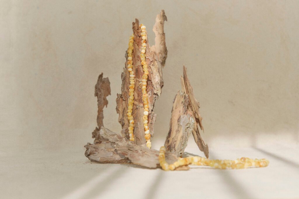 Pale amber necklace draped over a piece of driftwood against a light neutral backdrop