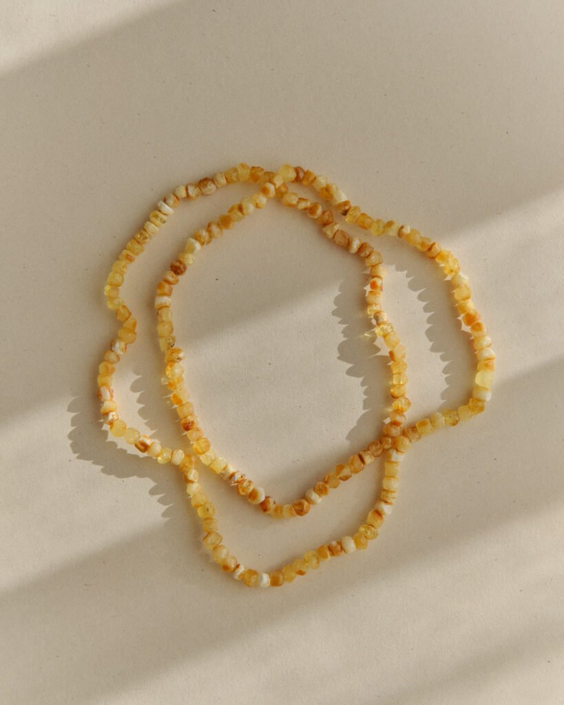 Pale amber necklace coiled into an overlapping loop on a sunlit surface with soft petal-shaped shadow