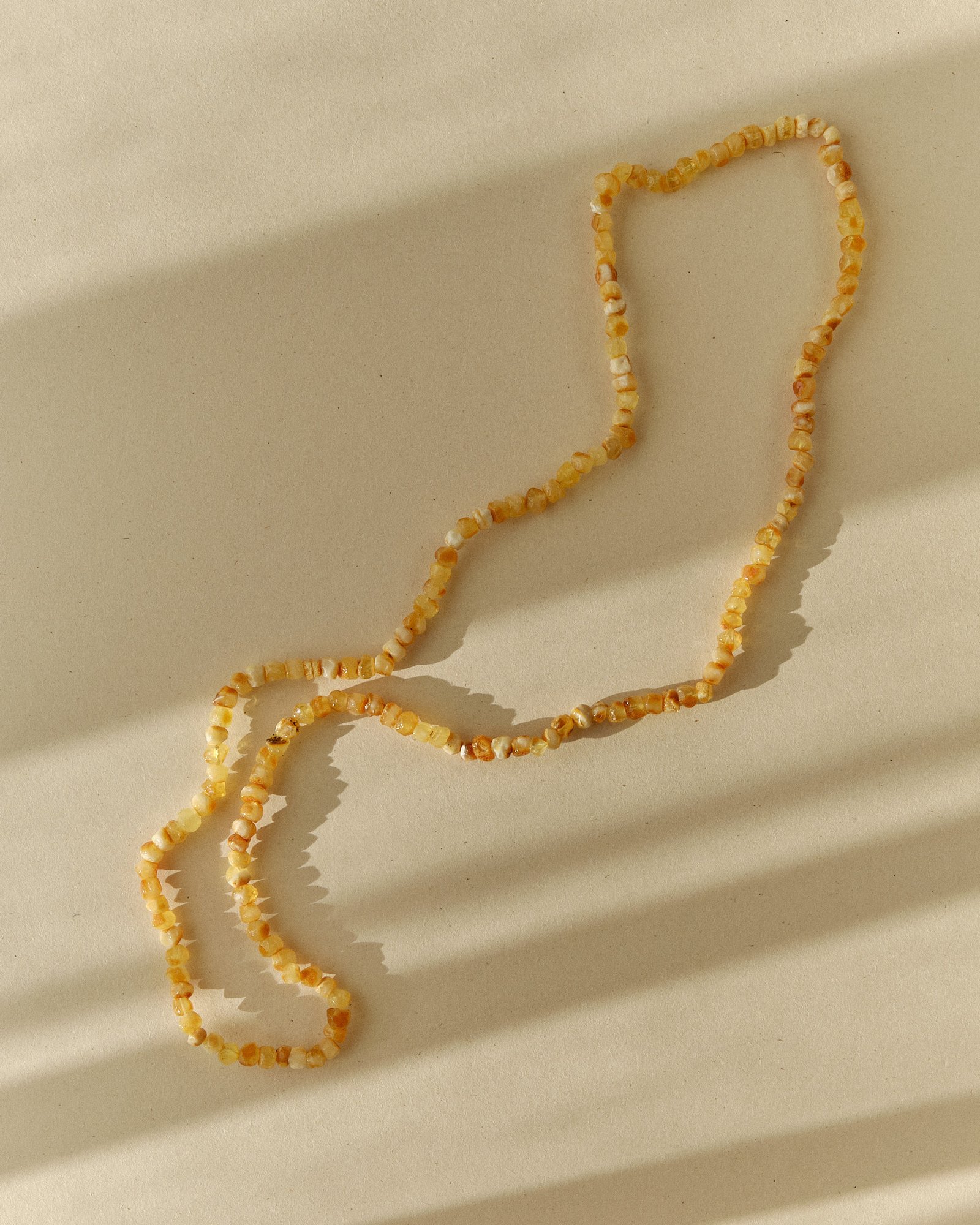 Pale amber necklace laid in loose curves on a sunlit surface with long streaked shadows