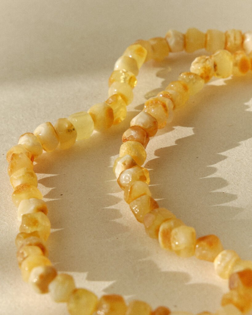 Close-up of a pale honey amber necklace laid in loops on a sunlit surface with sharp shadow