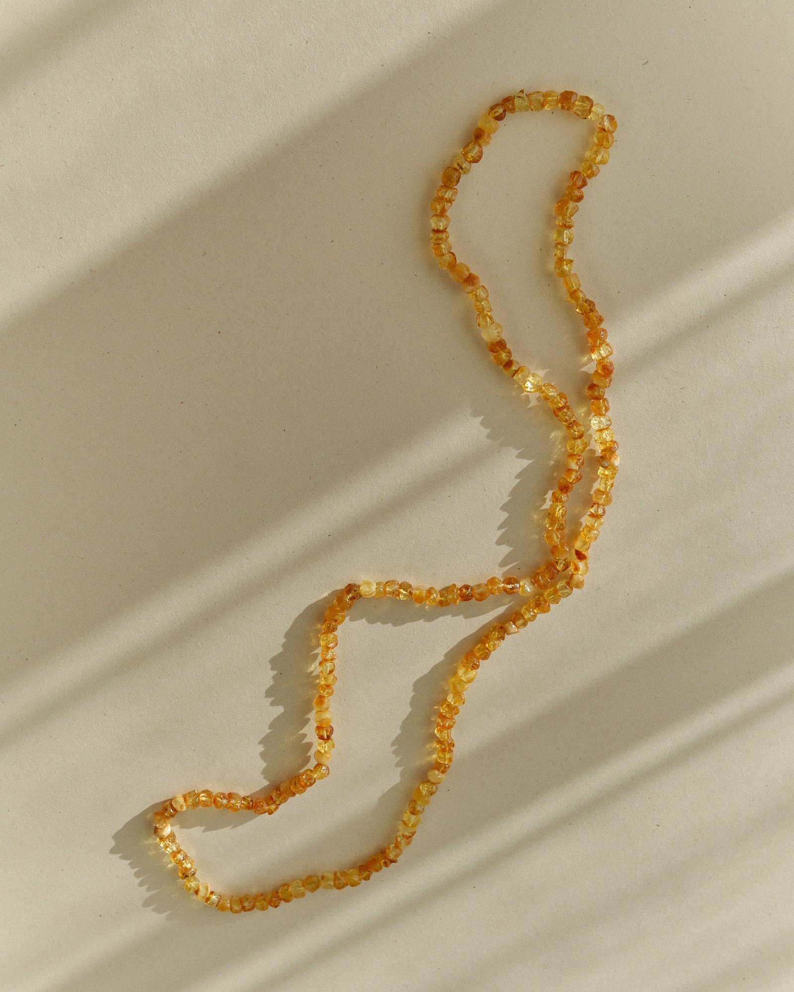 Golden amber necklace winding in a loose S shape on a sunlit surface with long streaked shadows