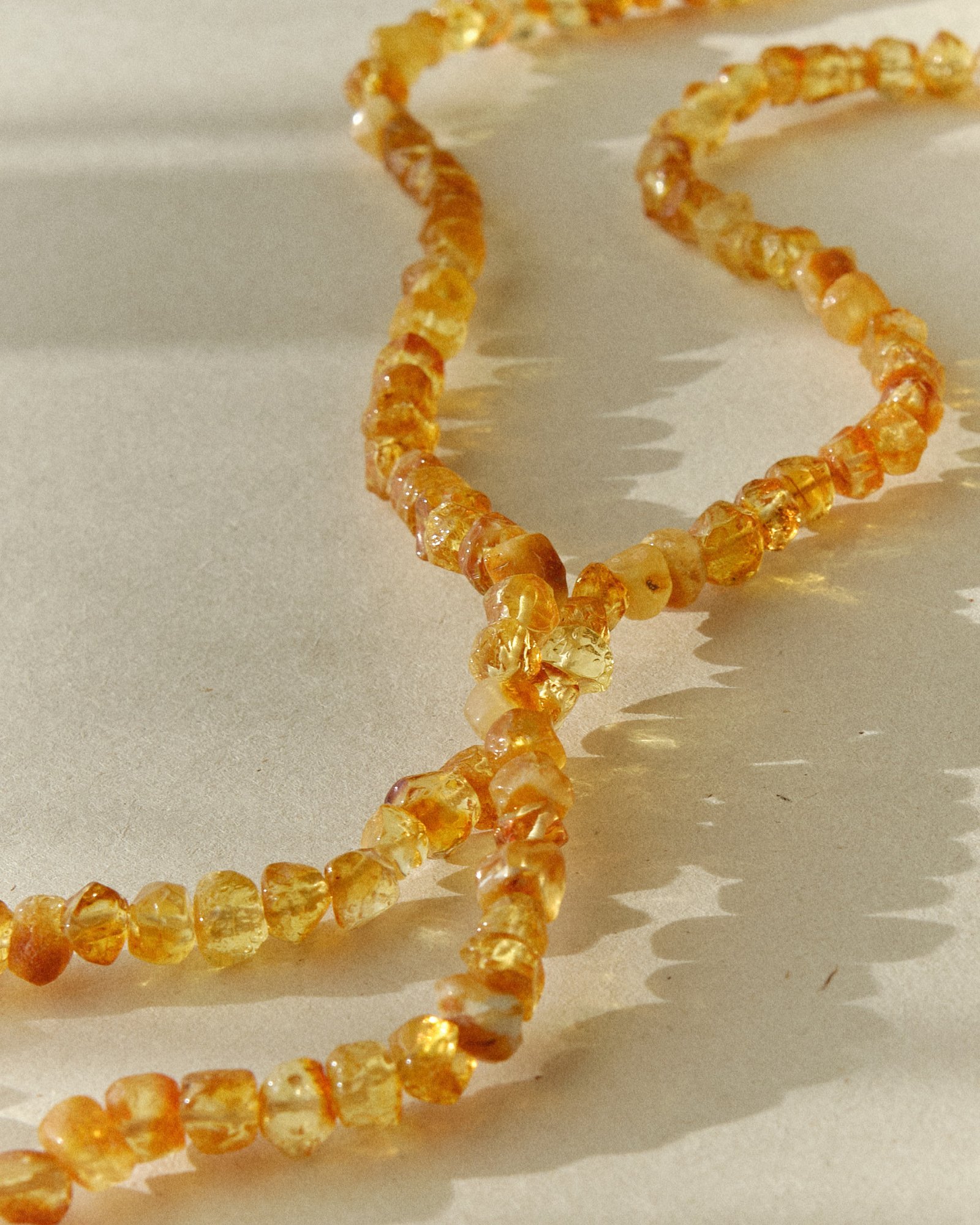 Close-up of a golden amber necklace laid in an S-curve on a sunlit surface with sharp shadow