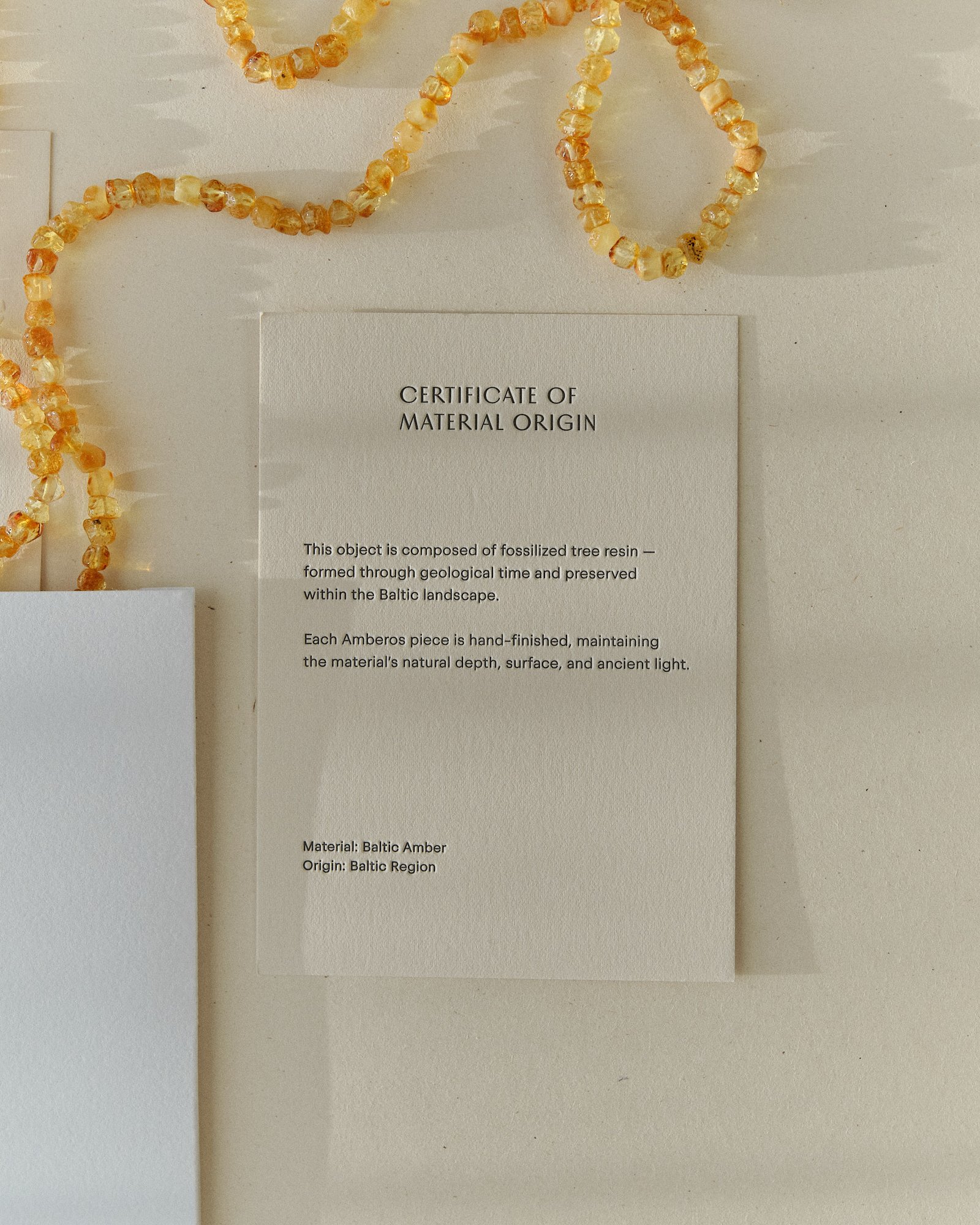 Honey amber necklace curled beside the Amberos certificate of material origin card and packaging box