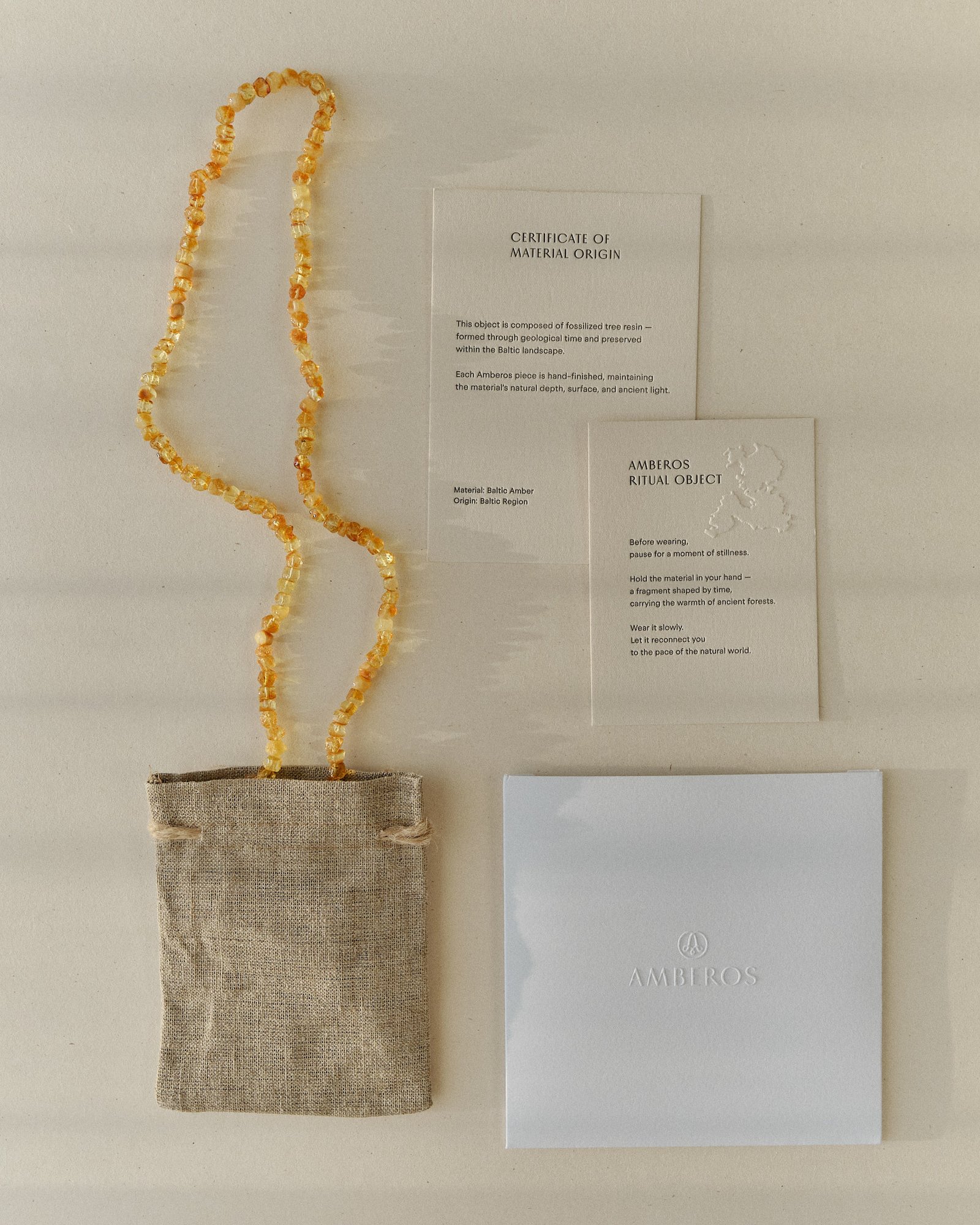 Honey amber necklace draped over the full Amberos packaging set of certificate card, ritual object card, linen pouch and box