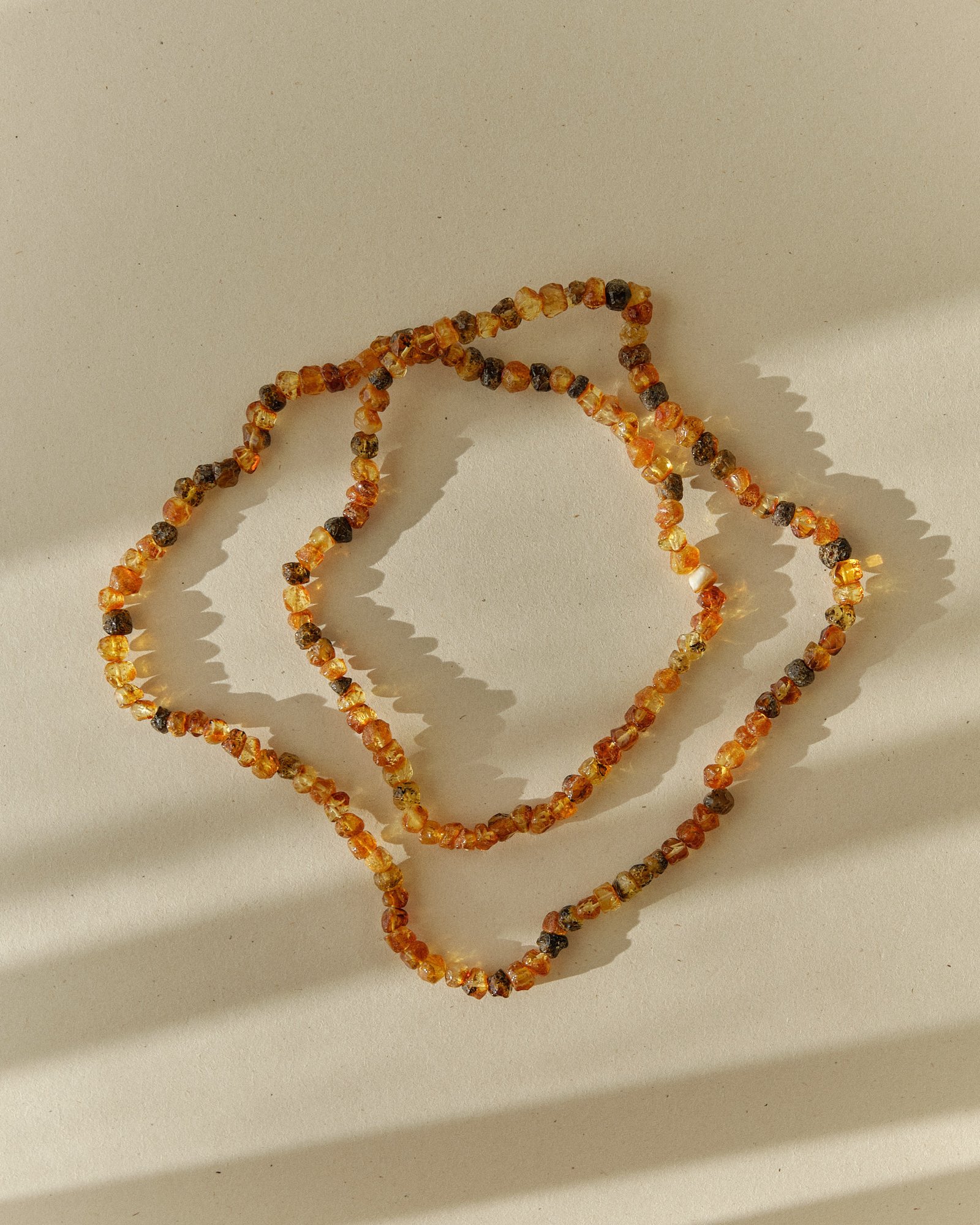 Cognac and dark amber necklace coiled into an overlapping loop on a sunlit surface with sharp shadow