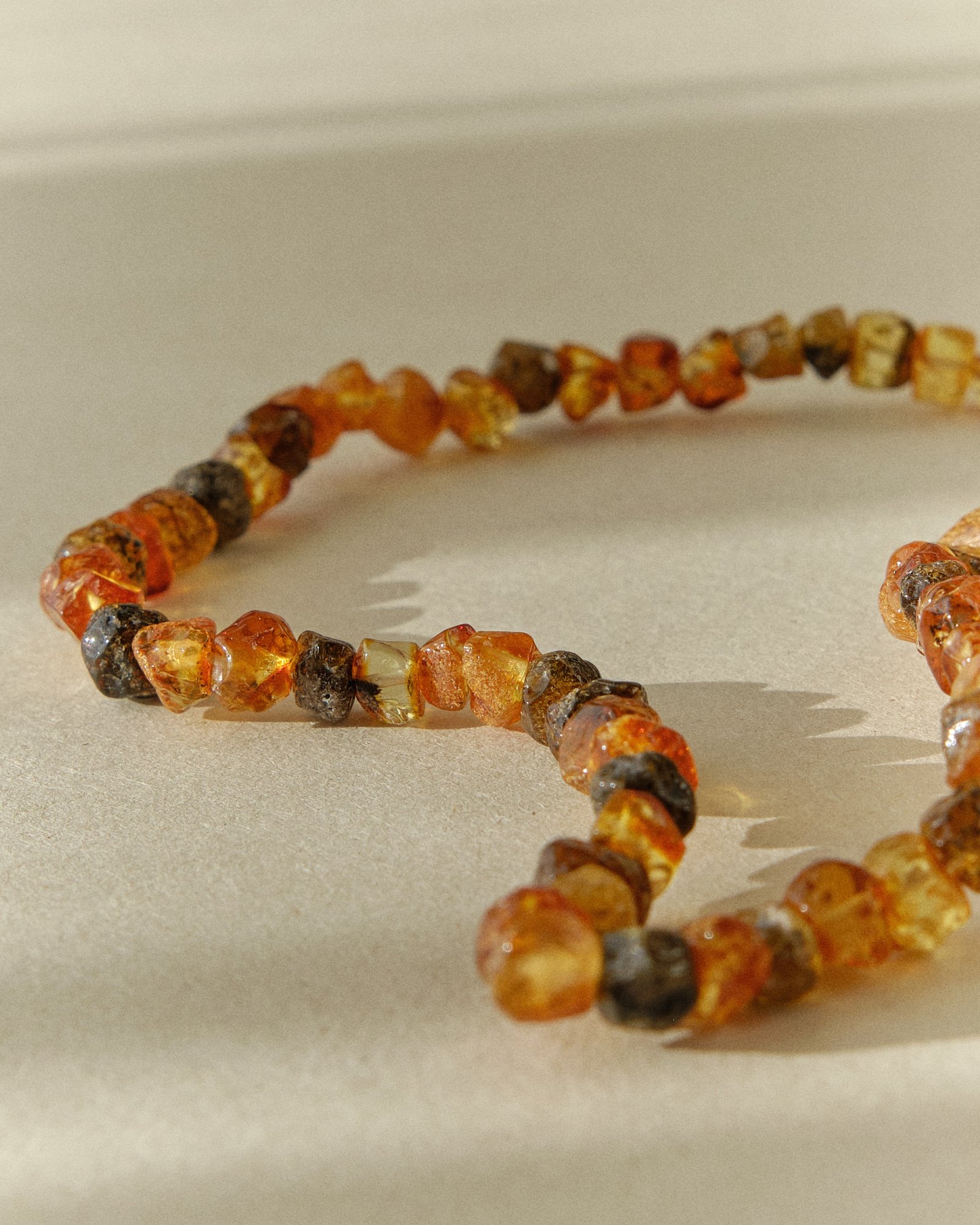 Close-up of a raw multicolor amber bracelet coiled into a loop on a textured surface
