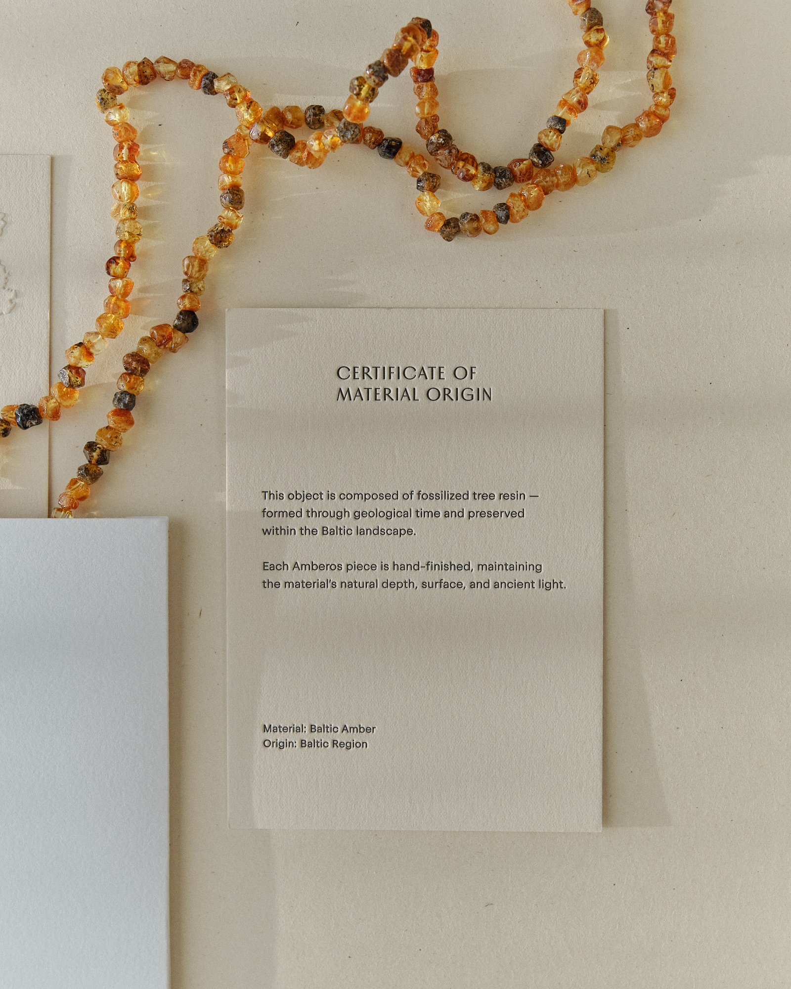 Cognac amber necklace draped over the Amberos certificate of material origin card and packaging box