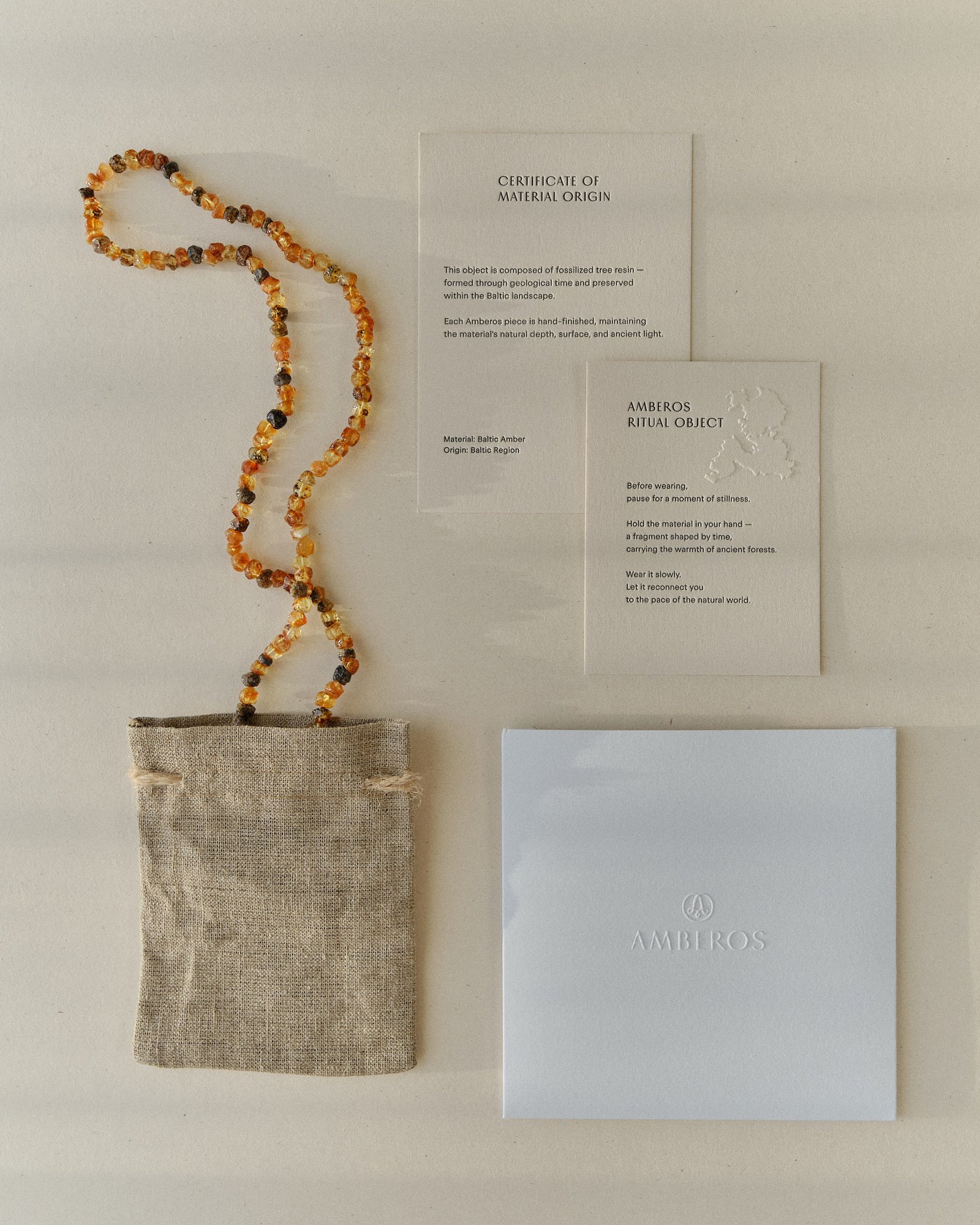 Cognac and dark amber necklace draped over the full Amberos packaging set, seen from above